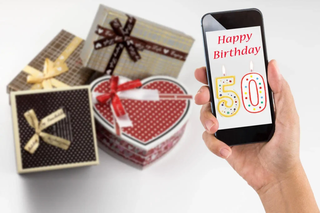 Happy 50th birthday wishes for WhatsApp with a smartphone displaying a birthday message beside a decorated cake.