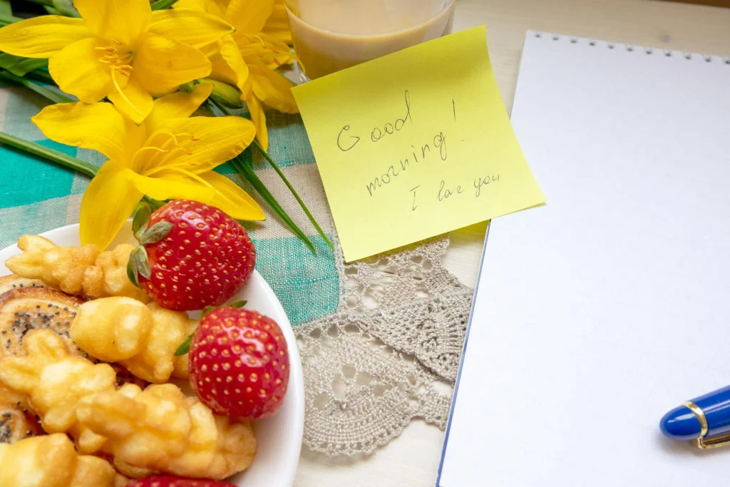 Good morning love messages for girlfriend with sweet compliments on a handwritten card beside flowers and breakfast.